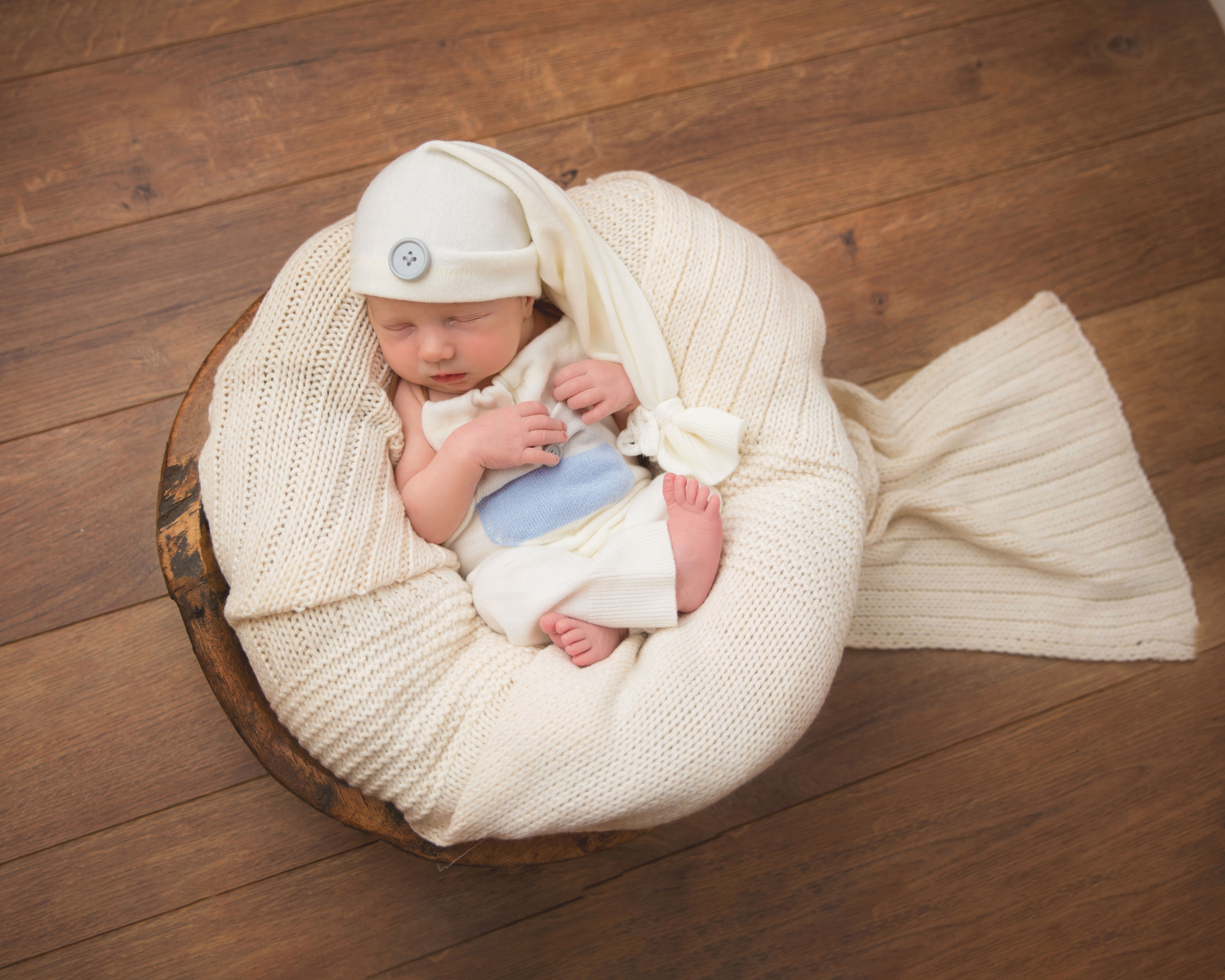 Wooden background, baby placed in curved natural position with light toned wraps