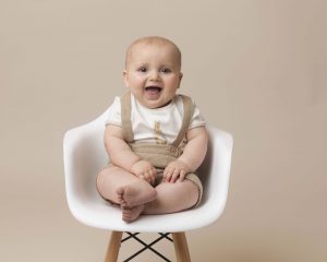 Little boy is posing a white chair with a big giggle.